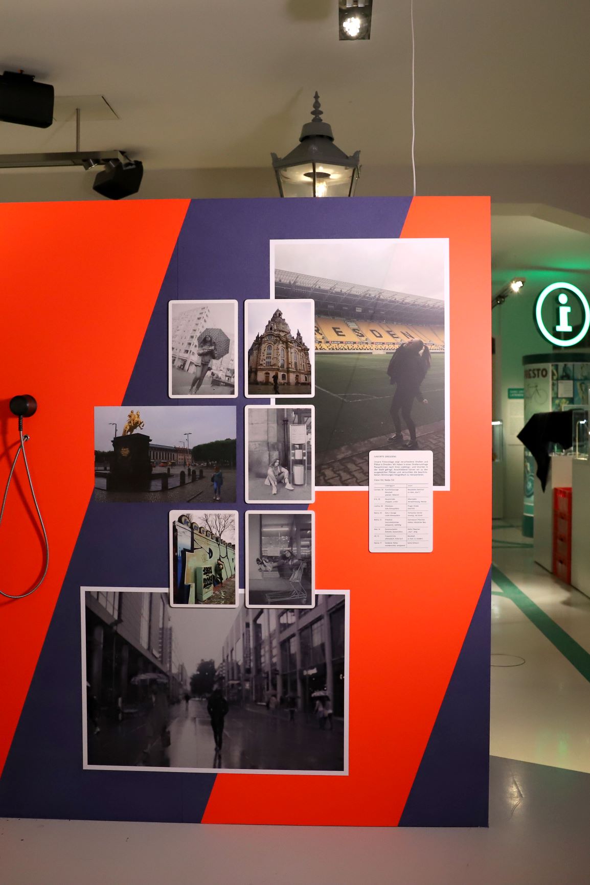 Auf einer blau-orange gestreiften Wand h&auml;ngen Fotos mit Orten in Dresden.