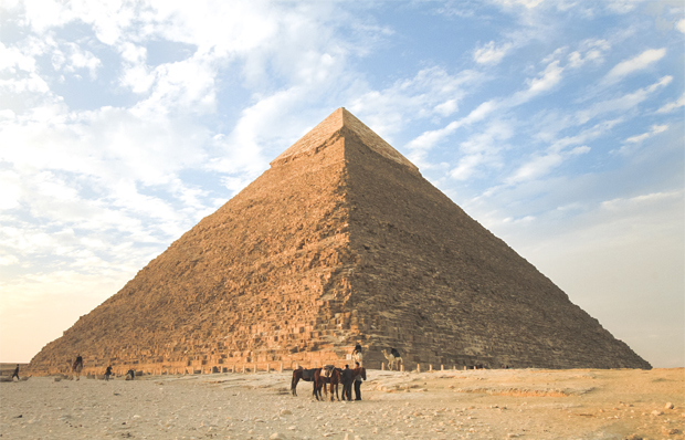 Foto einer ägyptischen Pyramide. Vor dem monumentalen, spitzen Grabbauwerk kann man ein paar Menschen und Maulesel erkennen.