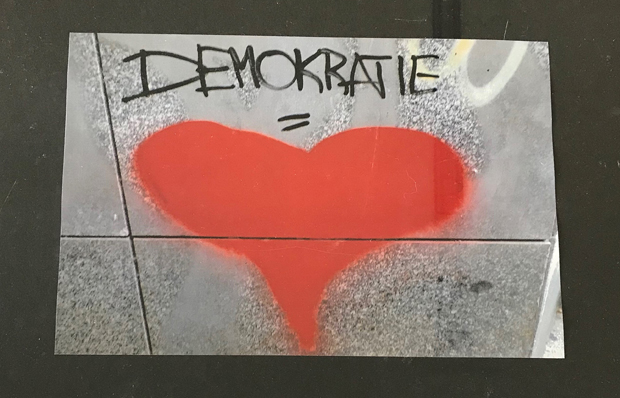 Picture of a wall with a big red heart and the word democracy sprayed on it.