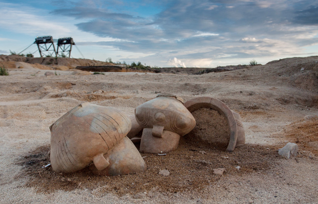 Das Foto zeigt drei prähistorische Gefäße, die noch zum Teil in der Erde stecken. Im Hintergrund sind Fördertürme für den Braunkohletagebau zu sehen.