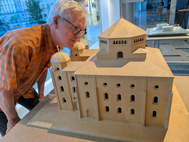 Ein &auml;lterer Herr beugt sich &uuml;ber das h&ouml;lzerne Architekturmodell einer Synagoge.