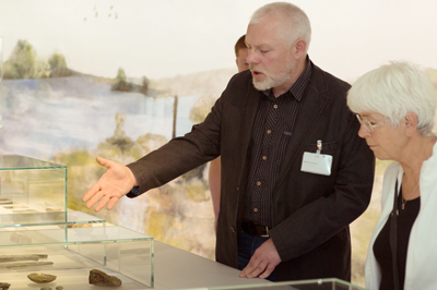Ein Ausstellungsmoderator erklärt einer Besucherin ein Objekt in der Ausstellung.