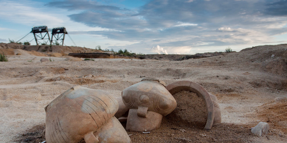 Foto mehrerer prähistorischer Gefäße im Sand. Im Hintergrund zwei Fördertürme