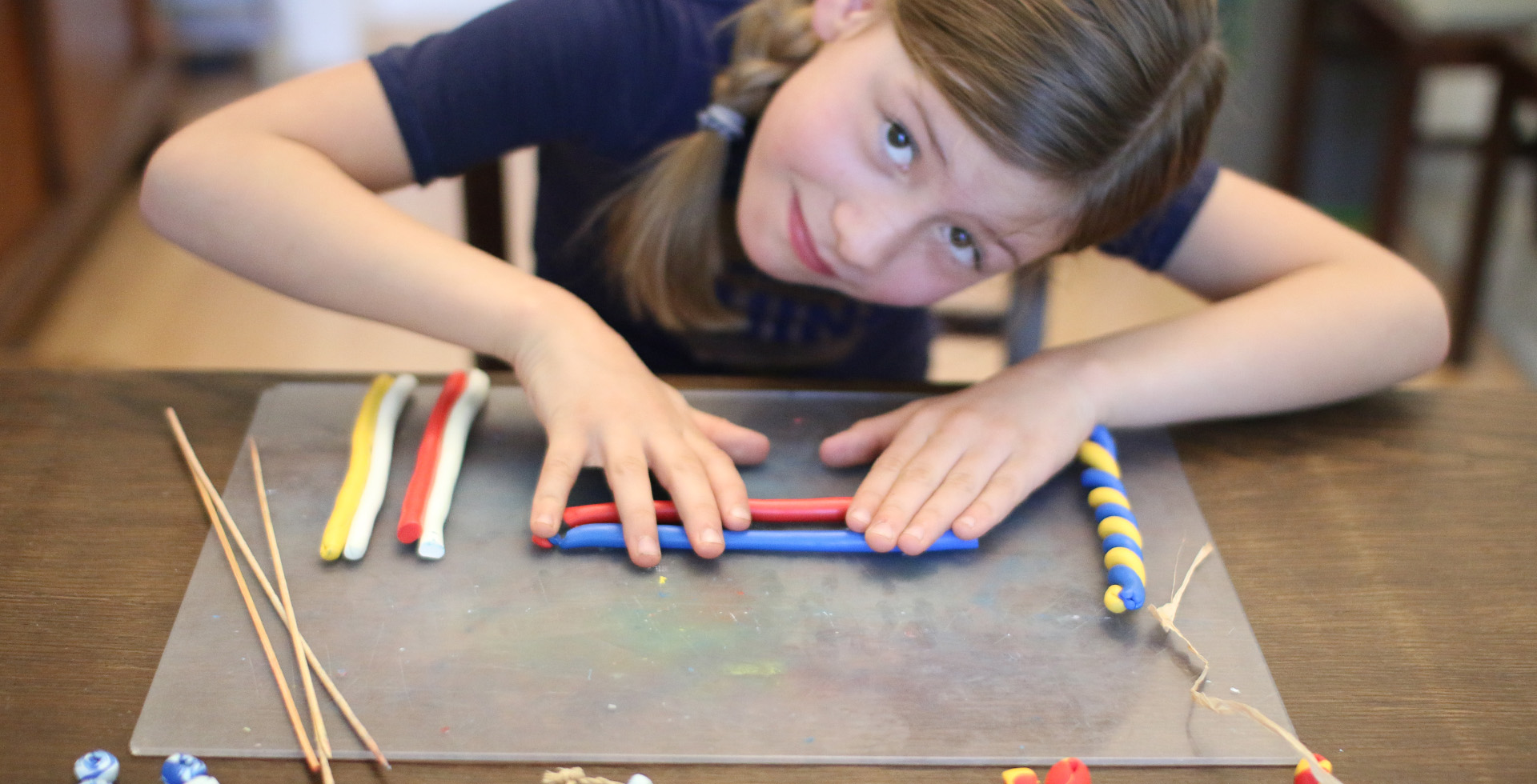 Ein Kind rollt zwei verschiedenfarbige Knetestränge auf einer Unterlage