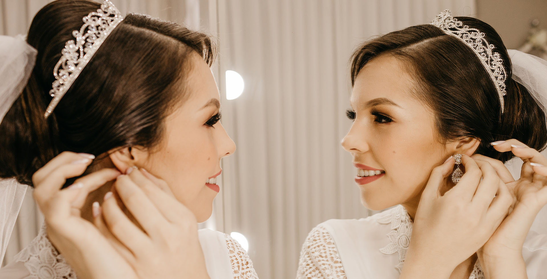 Eine junge Braut steckt sich vor dem Spiegel Ohrringe ein.