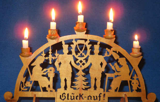 Foto eines hölzernen Schwibbogens mit Bergleute-Motiv und brennenden Kerzen.