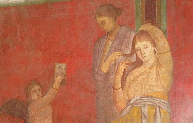 Römische Wandmalerei einer sitzenden Frau, deren Sklavin ihr die Haare frisiert. Ein Engel hält ihr ein Bild oder einen Spiegel hin.