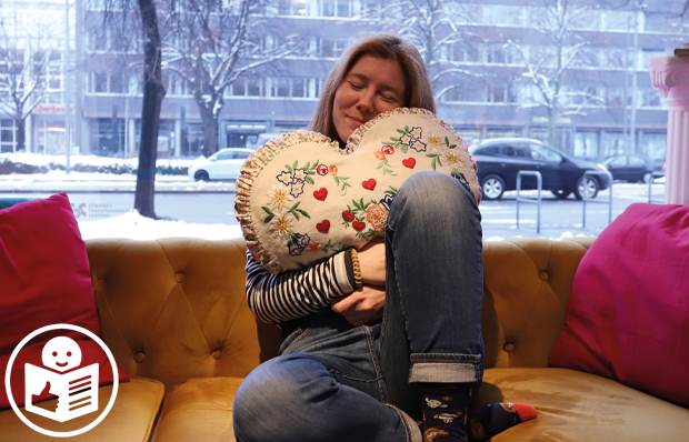 Foto einer jungen Frau, die auf einem Sofa sitzt und mit einem herzförmigen Kissen kuschelt.