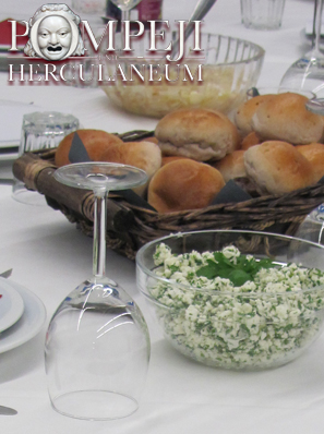 Foto eines festlich eingedeckten Tisches mit weißer Tischdecke, Tellern, Weingläsern, einer Schüssel mit Kräuterquark sowie einem Korb mit Brötchen.